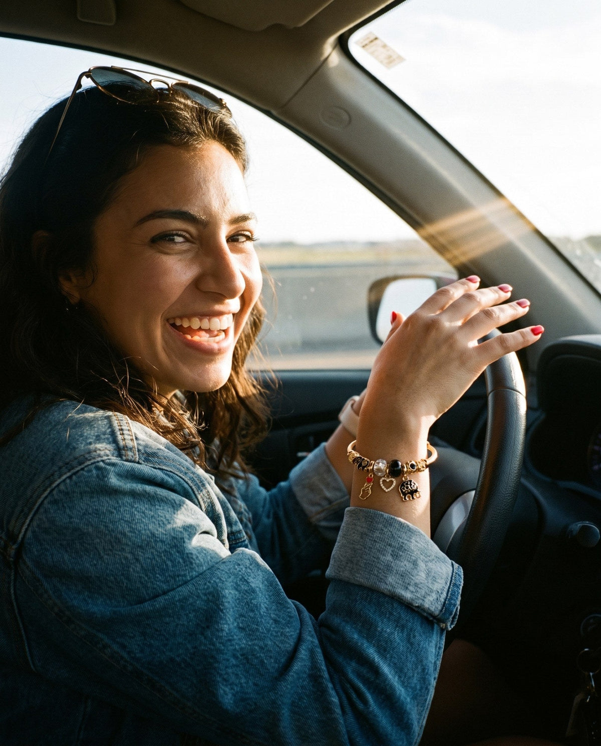 Young woman laughing in the drivers seat wearing a gold elephant charm bangle