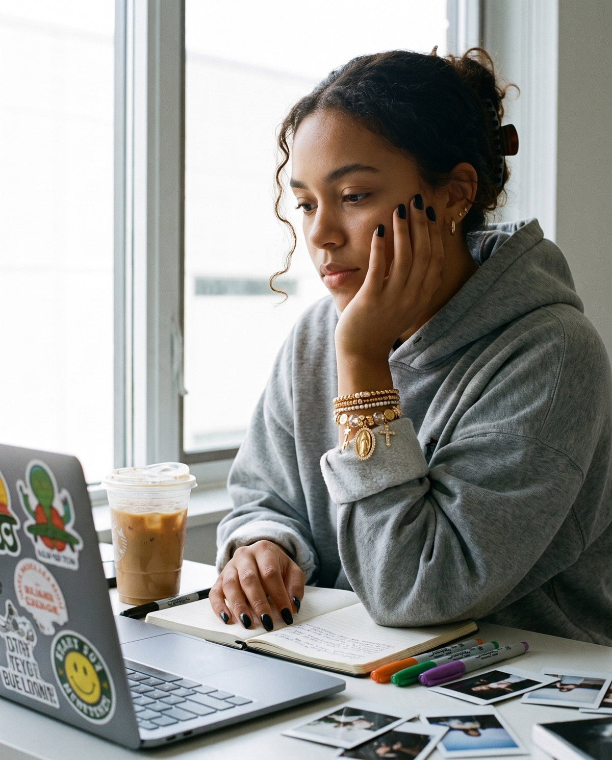 Young woman working at a desk by a window wearing a gold charm bangle