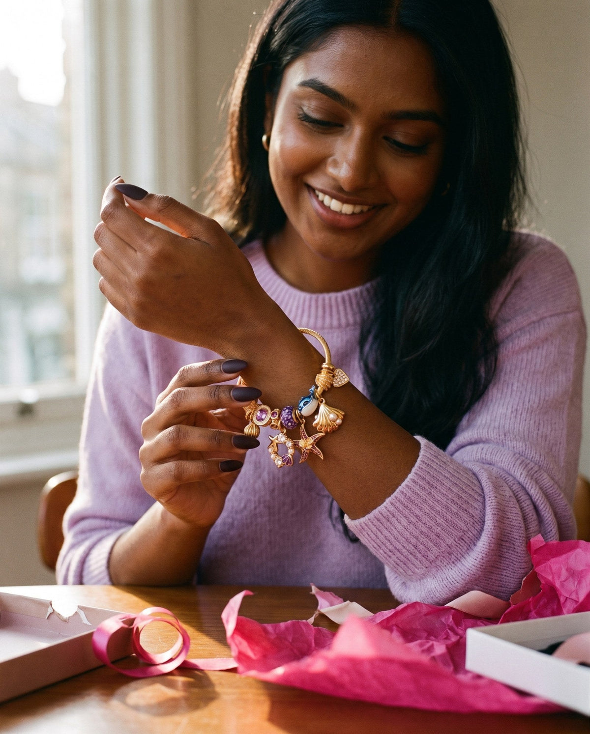Young woman smiling as she looks at a newly unwrapped gold charm bangle on her wrist